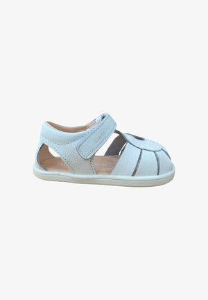 Sandalia de cuero blanca para niños pequeños con puntera cerrada, correa de velcro y laterales recortados sobre una suela de goma, mostrada de perfil sobre fondo blanco.