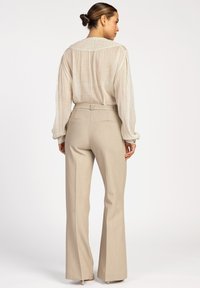 Beige textuur blouse met lange mouwen en een relaxte pasvorm, gecombineerd met strakke, lichtgekleurde broek met achterzakken en een gladde afwerking.