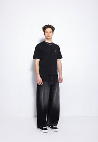 Czarny t-shirt z krótkim rękawem z małym logo na piersi, zestawiony z szerokimi czarnymi dżinsami o wyblakłym wykończeniu. Czarne sneakersy.