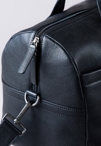 Black leather bag featuring a rounded shape, visible zipper, metal hardware, and textured surface with subtle stitching details.