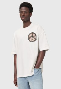 Overdimensioneret creme t-shirt med et rundt leopardprint grafisk design og sort tekst på brystet. Korte ærmer, blødt stof, afslappet pasform.