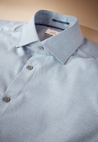 Világoskék, gombos ing, kis kockás mintával, hegyes gallérral és szürke gombokkal. A címkén a "Next Signature" márkanév látható.