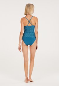 Tankini-top in diep teal met een geweven patroon en gekruiste bandjes. Gecombineerd met bijpassende lage slipjes. Glad, rekbaar materiaal.