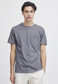 Tricou gri cu mânecă scurtă, realizat dintr-un material moale, având un guler rotund și un buzunar pe pieptul stâng. Textură netedă, croială lejeră.