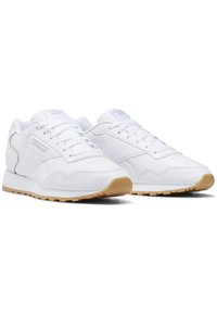 Zapatillas deportivas blancas con parte superior de cuero liso, punta redondeada, diseño de cordones y suela de goma. Marca en los laterales.