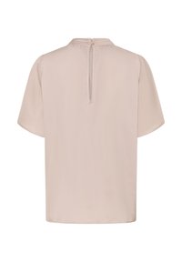 Blouse à manches courtes en beige clair, présentant un subtil éclat, un col rond et une fermeture à clef au dos agrémentée de deux boutons.