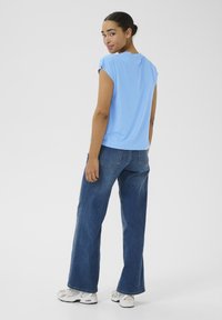 Top scurt, de culoare albastru deschis, cu un croi lejer, asortat cu blugi închiși la culoare, cu talie înaltă și picior larg, purtați cu adidași albi. Design simplu, fără modele.