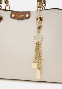 Sac à main gris clair avec des accents marron, quincaillerie dorée, détails en chaîne et un petit cadenas. Présente une surface texturée et des poignées doubles.