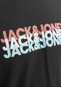 T-shirt nera con testo audace e sovrapposto in rosa, bianco e azzurro che legge "JACK & JONES" in diverse dimensioni e posizioni. Texture liscia.