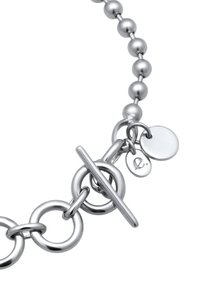 Bracelet en argent composé de perles rondes et d'anneaux circulaires liés, avec un fermoir à bascule et deux petits pendentifs, dont l'un est gravé, finition polie.