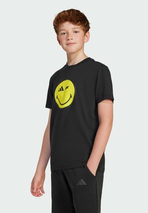 T-shirt nera a maniche corte con una grande grafica di una faccina sorridente gialla. Realizzata in materiale morbido, abbinata a pantaloni sportivi neri.