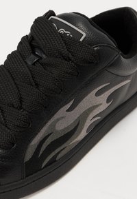 Sneaker nera in pelle texture, con spesse stringhe nere e un motivo a fiamma grigio di lato. Suola in gomma liscia.
