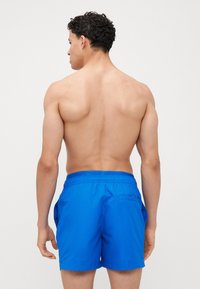 Blauwe zwembroek met een elastische tailleband, voorzien van zijzakken en een enkele achterzak. Gemaakt van glad, snel drogend materiaal.
