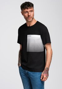 Černé tričko s krátkými rukávy a klasickým výstřihem, na hrudi s bílým vodorovným pruhovaným vzorem. Vyrobeno z bavlny.