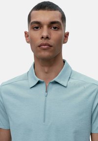 Lyseblå kortermet polo-skjorte med glidelås i kragen, strukturert stoff og minimale designdetaljer på skulderen.