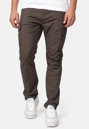 Cargo pants in dark brown cotton, featuring side pockets, tapered fit, and visible stitching details. Paired with light-colored sneakers.