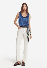 Mörkblå satinklänning utan ärm, vita linnibyxor, brun läderbälte och mörkbruna flätade sandaler. Tillbehör inkluderar en mönstrad scarf knuten i midjan.