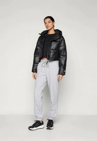 Melnā, sagrieztā pūkaina jaka ar tekstūru, pelēkas sporta bikses ar elastīgiem galiem un melnas kedas ar baltām zolem.