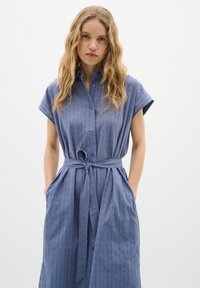 Rochie cămașă de culoare albastru deschis, cu mâneci scurte, talie curea, închidere cu nasturi, țesătură texturată cu linii verticale, buzunare laterale.