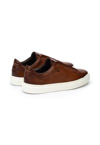 Zapatos de piel marrón tipo slip-on con una suela de goma blanca, que presentan costuras mínimas y un sutil logo en el talón y el lateral.