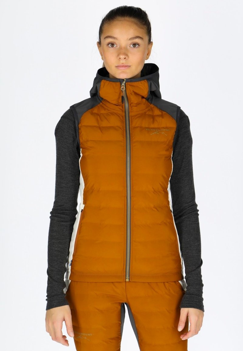 Gilet imbottito arancione con colletto alto e zip, caratterizzato da dettagli neri e una vestibilità aderente. Indossato sopra una maglietta grigia a maniche lunghe.