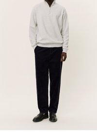 Lichtgrijze ritsvest met een ribbelonderrand, gecombineerd met donkerblauwe corduroypants en zwarte schoenen. Soepele texturen en een ontspannen pasvorm.