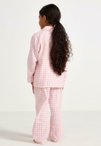 Lyserød ternet pyjamas sæt med en skjorte med lange ærmer og matchende brede bukser, lavet af blødt stof.