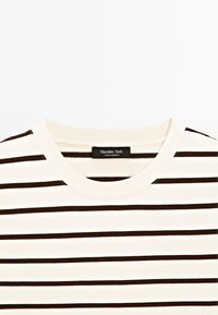 Cremefarbenes Baumwoll-T-Shirt mit horizontalen dunkelbraunen Streifen, einem runden Ausschnitt und einem Etikett, das innen im Ausschnitt genäht ist.