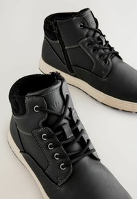 Schwarze Leder-Ankle-Boots mit vorderen Schnürsenkeln, seitlichem Reißverschluss und Fleece-Futter. Kontrastnähte und Gummisohle.