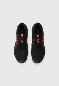 Baskets de sport noires avec dessus en maille et accents rouges. Bout arrondi, surface texturée et semelle blanche avec des lacets en haut.