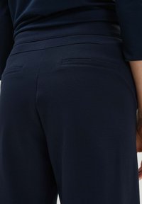Pantalons bleu marine avec une texture douce et lisse, dotés de deux poches arrière et d'une taille ajustée pour un look sur mesure.