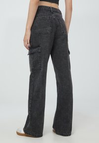 Czarne, szerokie spodnie cargo z miękkiego, teksturowanego denimu; posiadają wiele kieszeni i wysoką talię.