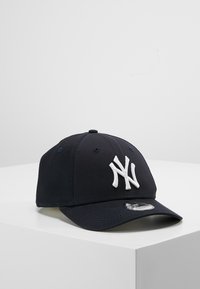 Tengerészeti baseball sapka fehér, emelt "NY" logóval az elején. Ívelt karimával és állítható pánttal a hátulján rendelkezik. Pamut anyagból készült.