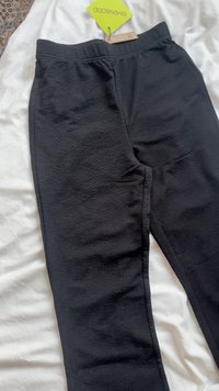 Mustad, tekstureeritud jogger püksid elastse vöökohtaga, millel on kitsas lõige ja külgõmbluse detailid, asetatud valgele pinnale.