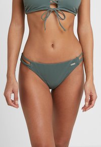 Bikini w kolorze morskiej zieleni, z dwoma bocznymi paskami, minimalnym zakryciem, gładką teksturą i małym logo z przodu po prawej stronie.