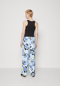 Top senza maniche nero abbinato a pantaloni a gamba larga con uno sfondo blu pastello e grandi pattern floreali blu e neri.