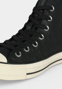 Μαύρο sneaker ψηλής φιάλης με μαύρα κορδόνια, μεταλλικά ροδέλες, υφή στο πλάι και λευκή λαστιχένια σόλα με μαύρη ρίγα.
