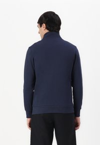 Sudadera de tiro alto en color navy, con cuello alto, puños y dobladillo acanalados. Textura suave con diseño minimalista, mostrada desde la parte posterior.