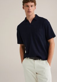 Polo de navy cu mânecă scurtă, cu un model texturat, având un guler cu decupaj și un buzunar pe piept, asortat cu pantaloni de culoare deschisă.