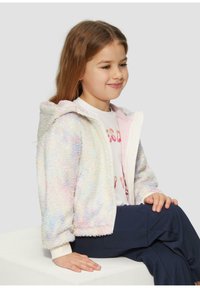 Flauschige, pastellfarbene Regenbogenjacke mit einem Reißverschluss vorne, Kapuze und gerippten Bündchen. Getragen über einem weißen Hemd und einer marineblauen Hose. Glatte Textur.