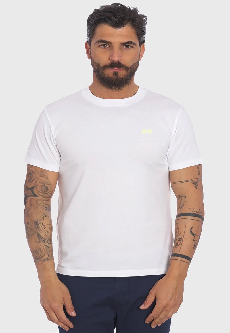 T-shirt bianca a maniche corte con scollatura rotonda e un piccolo logo giallo sul petto. Presenta un tessuto morbido e una vestibilità classica.