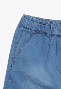 Pantaloni in denim con cintura elastica blu, dotati di tasche frontali e passanti per cintura, che evidenziano la sezione superiore sinistra e i dettagli della cucitura.