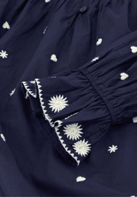 Marineblaues Kleid mit weißen bestickten Mustern. Hat gepuffte Ärmel mit elastischen Säumen und floralen Designs am Saum. Knöpfe am Ausschnitt.