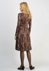 Pitkähihainen, tummanpunaisilla, ruskeilla ja kermanvärisillä paisley-kuvioilla varustettu mekko; kapea vyötärö, kellotettu hame, yhdistettynä mustiin kenkiin ja leggingsiin.