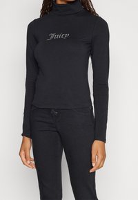 Black long-sleeve turtleneck top made of soft fabric, featuring a fitted design and a rhinestone "Juicy" logo on the front.
