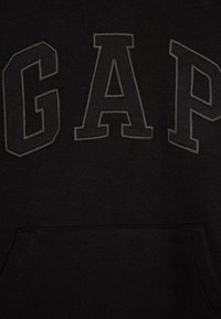Čierna mikina s kapucňou s veľkým šedým nápisom "GAP". Vyrobená z mäkkého textilu s prednou vreckom a rebrovaným lemom. Jednoduchý a klasický dizajn.