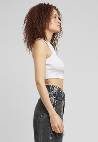 Hvit ribbet crop topp parret med svarte acid-wash høy midje jeans. Toppen har brede armhull; jeansene har en falmet tekstur.