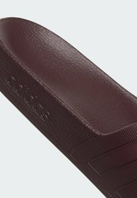Gros plan d’une sandale Adidas marron foncé avec une semelle texturée et le logo Adidas embossé sur le côté.