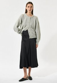 Lichtgrijze gebreide cardigan met een ronde hals, knoopsluiting en opengewerkte details. Gecombineerd met een zwarte satijnen middellange rok.