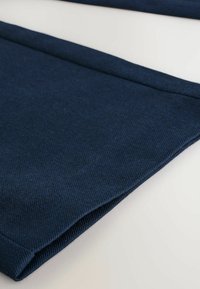Marineblaue Stoff mit einer strukturierten Oberfläche, die gefaltete Kanten und eine glatte Oberfläche zeigt, diagonal vor einem hellen Hintergrund platziert.